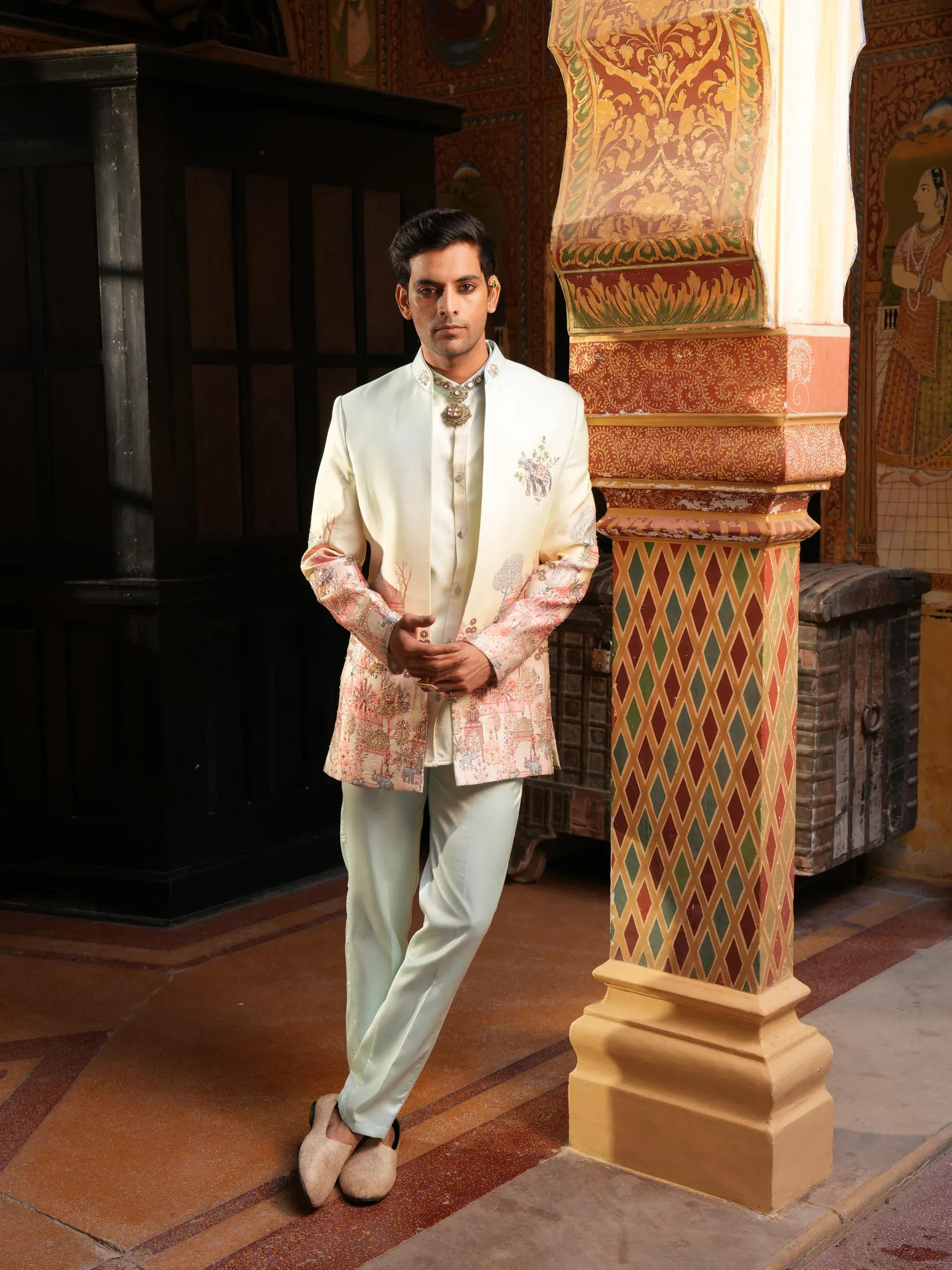 Model in an ivory bandhgala with a hand-painted sleeve panel, standing beside a frescoed pillar